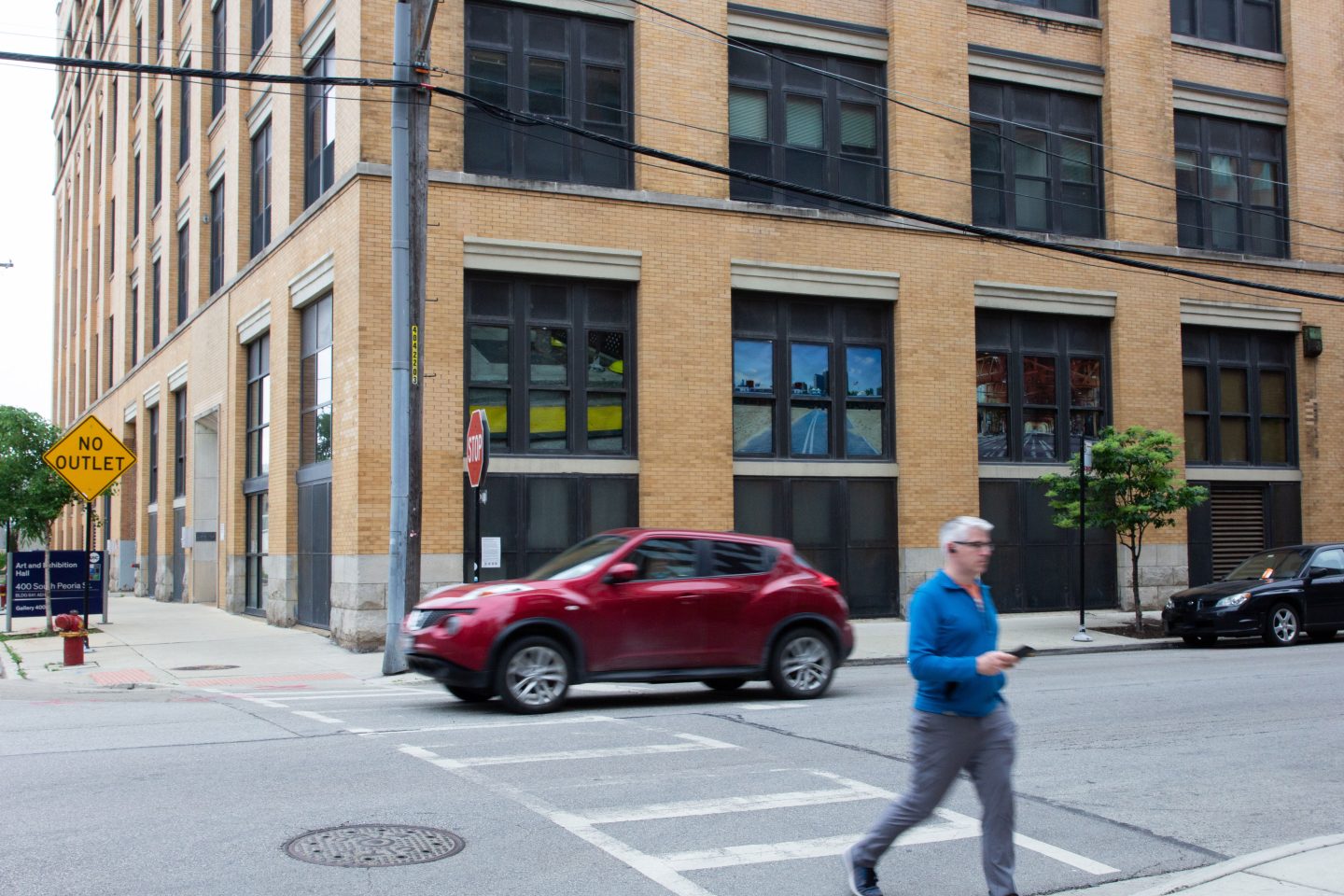 A red car and a person are crossing the street in front of the corner of a building.